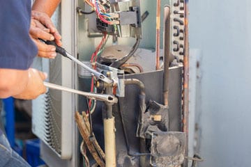 Two men holding wrenches and working on a home furnace.