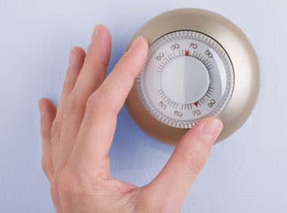 A hand turning the dial of a thermostat.