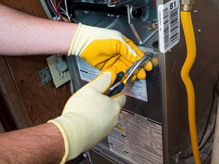 A man wearing yellow work gloves and holding a wrench to tighten a heating valve.