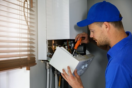 A man in a blue baseball cap and shirt holding an orange handled screwdriver in his right hand tightening a screw and cusping a panel in his left hand.