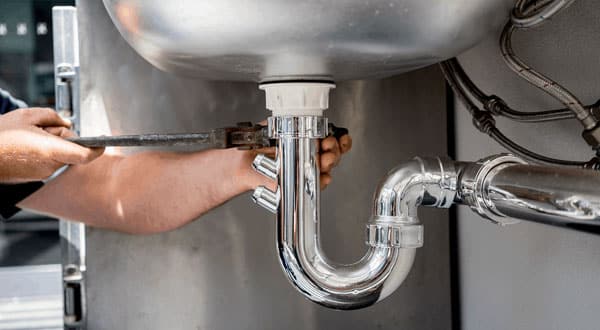 Man's hands holding a wrench and tightening a pipe nut on a sink.