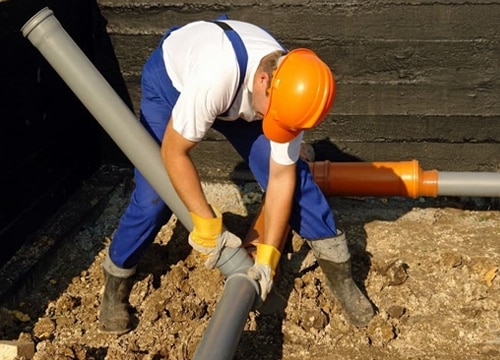 A man in an orange hardhat holding pushing one large sewer pipe into another