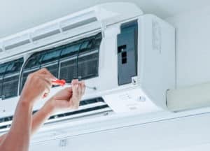 Woman's hands holding a screw driver tightening a screw on a Ductless mini splits air conditioner.