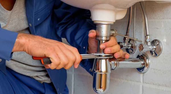 Man holding a wrench and tightening a bolt on a sink.